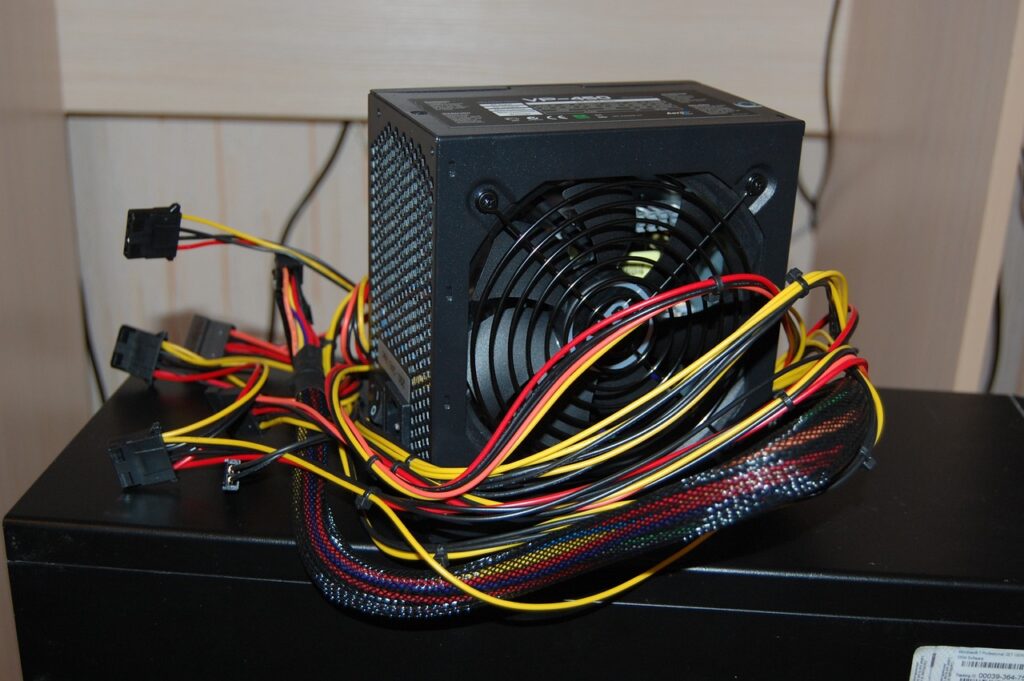 Power supply unit showing of computer laid over a wooden table against a white wall as the background. Concept image for electricity and power consumption of a gaming PC.