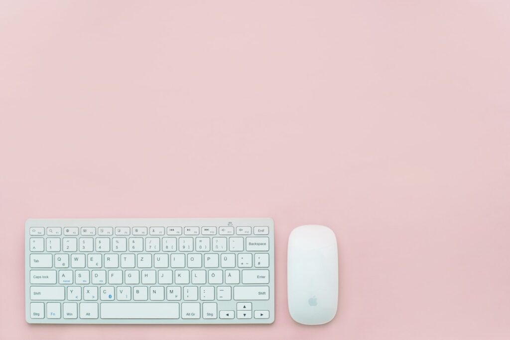 Apple keyboard and mouse placed over a pink background table. Concept image of keyboard and mouse positioning.