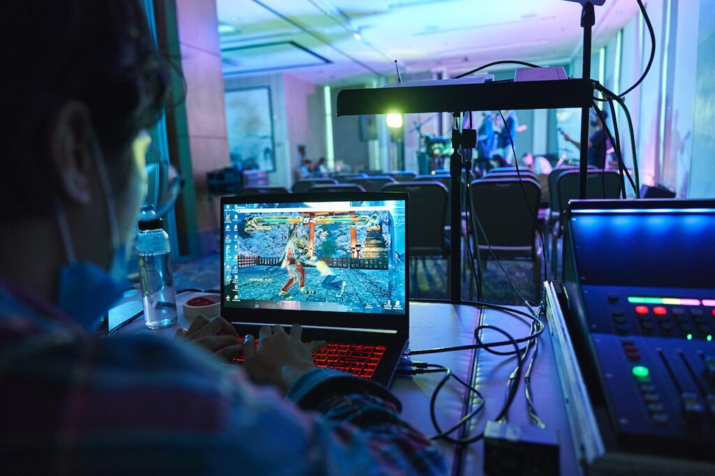 A man playing a fighting game on a gaming laptops in a neon-themed room. Concept image of why gaming laptops are cheaper than business laptops.