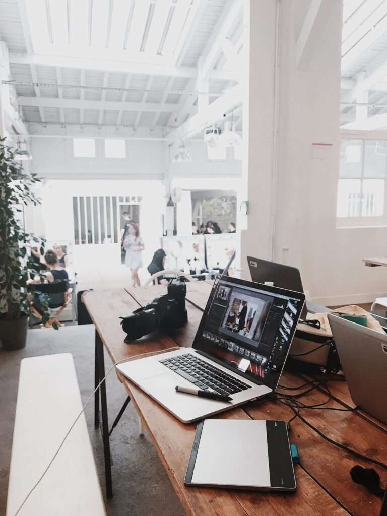 A MacBook business laptop and other electronic gadgets and laptops are lying on a wooden table. Concept image for why gaming laptops are cheaper than business laptop.  