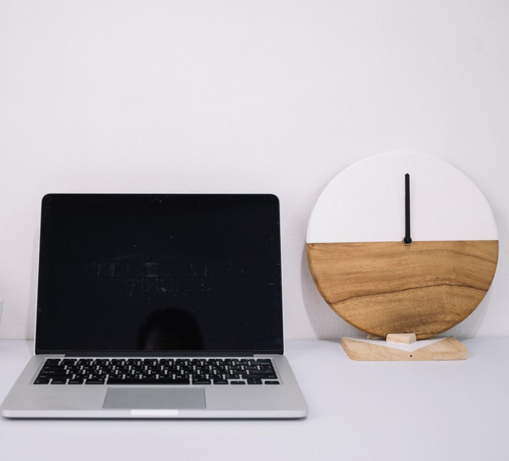 A regular laptop placed on a white table along with a clock.