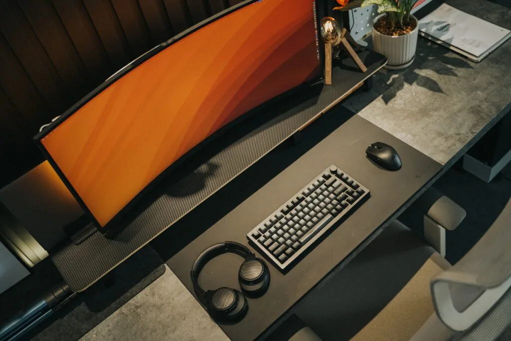 A curved gaming monitor on a desk with keyboard, mouse and headphones