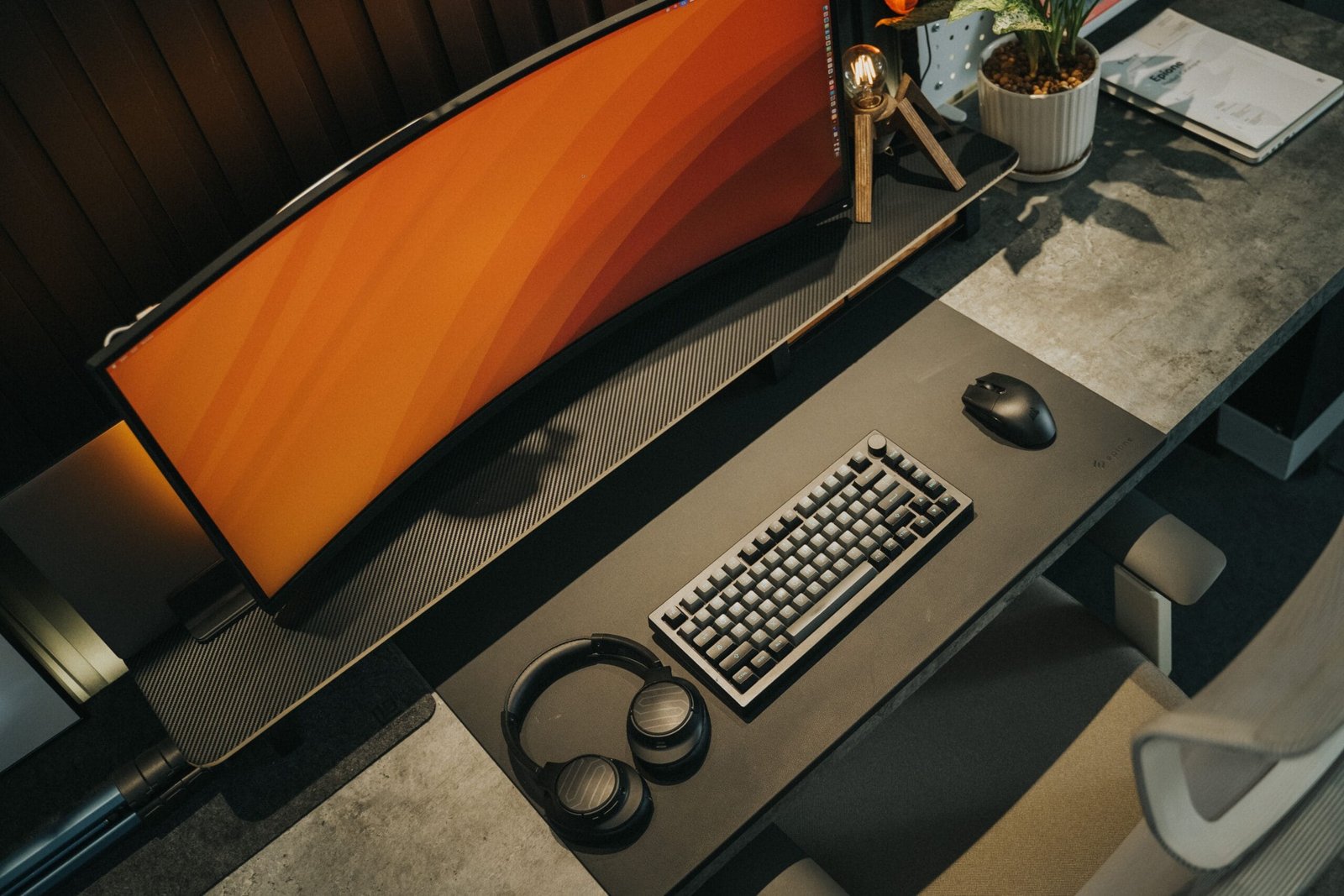 A curved gaming monitor on a desk with keyboard, mouse and headphones