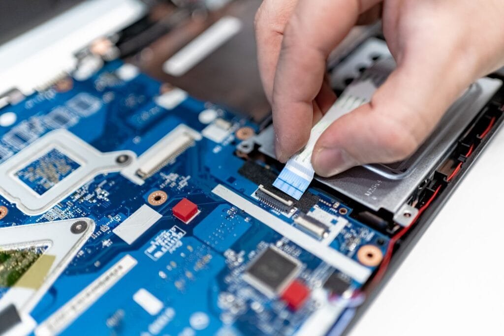 Technician disconnecting a ribbon cable on an opened laptop motherboard during a repair